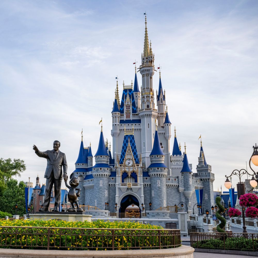 A statue of Walt Disney and Mickey Mouse in front of Cinderella Castle