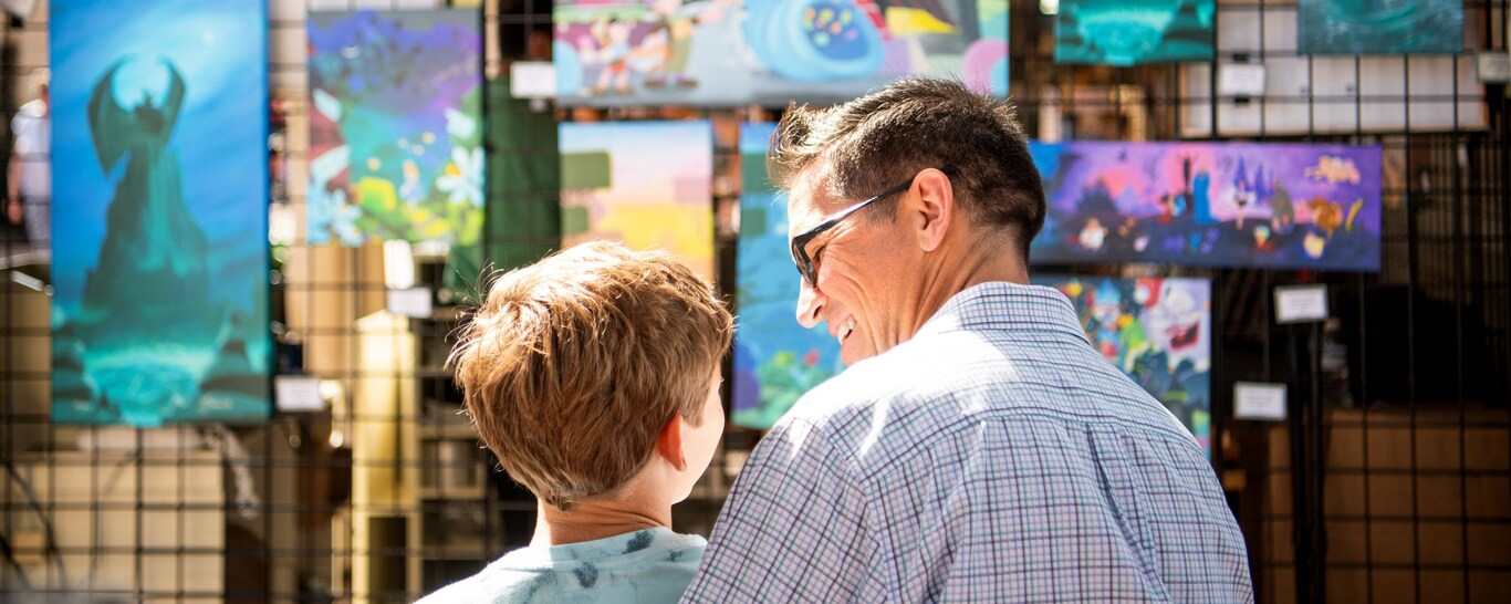 An adult and child gazing at artwork on display featuring various Disney characters