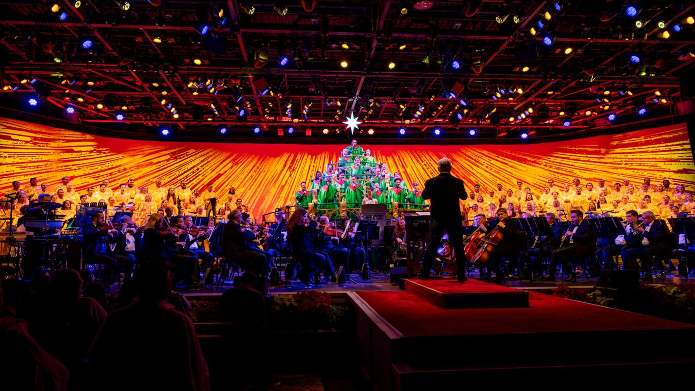 A conductor directing an orchestra and a choir, with some choir members dressed and arranged to look like a Christmas tree at the Candlelight Processional