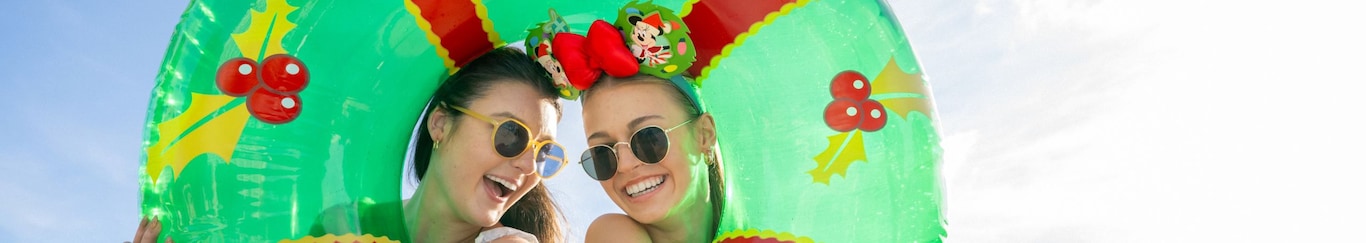 Two women peeking through and embracing an inner tube decorated to look like a Christmas wreath