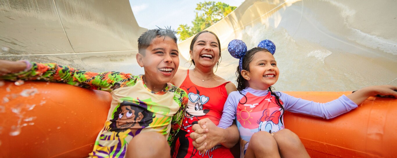 A mother and her 2 kids, all wearing Disney swimwear, gliding down a waterslide at the Miss Adventure Falls attraction at Disney's Blizzard Beach water park