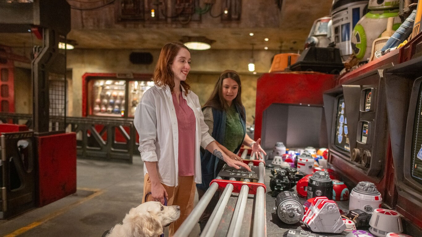 A woman reads the braille instructions for building a droid at the Droid Depot, while a female Cast Member looks on.