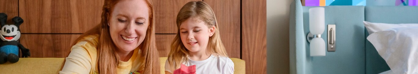 Mother and daughter enjoying a fruit snack together, sitting on a sofa at a Disneyland Resort hotel. 
