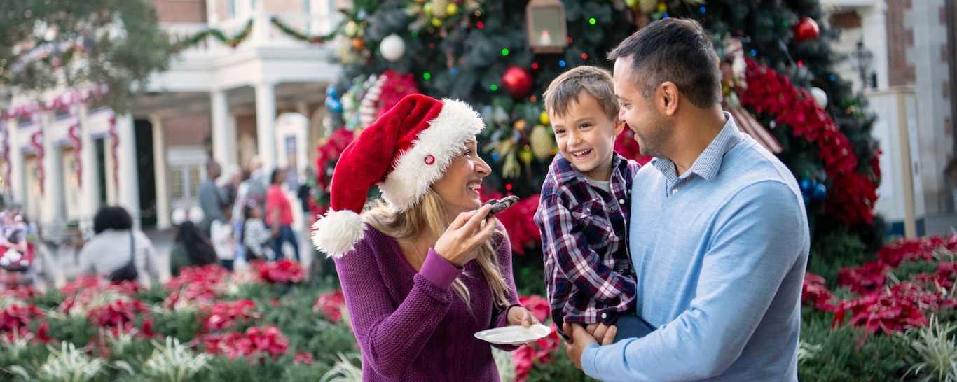 Two parents and their son eating Christmas cookies in front of the Christmas tree on Main Street, USA