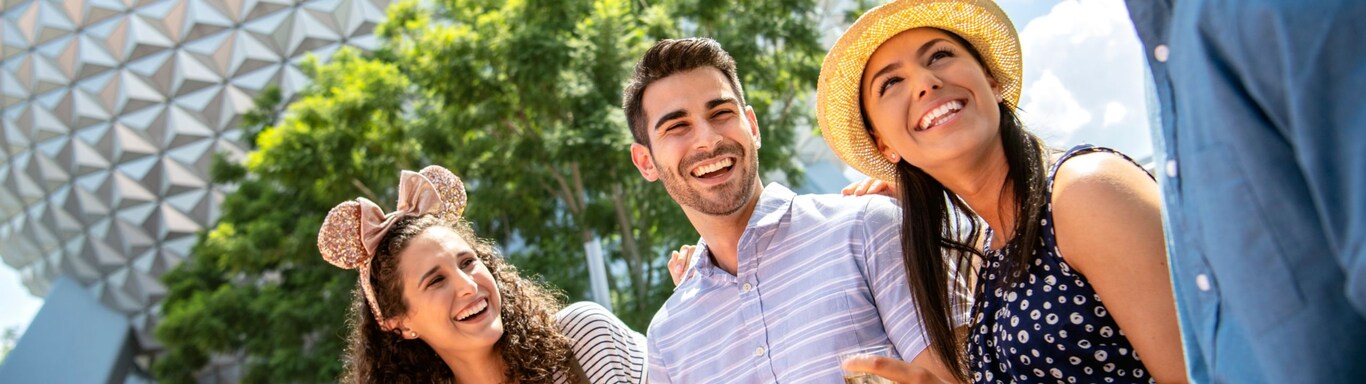 Un grupo de 4 amigos sonríe mientras disfruta de comida y bebida del festival cerca de Spaceship Earth en EPCOT  
