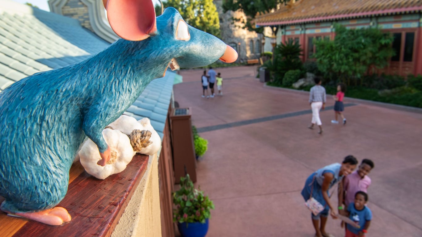 A family smiles up at a figure of Remy from Ratatouille perched on a roof