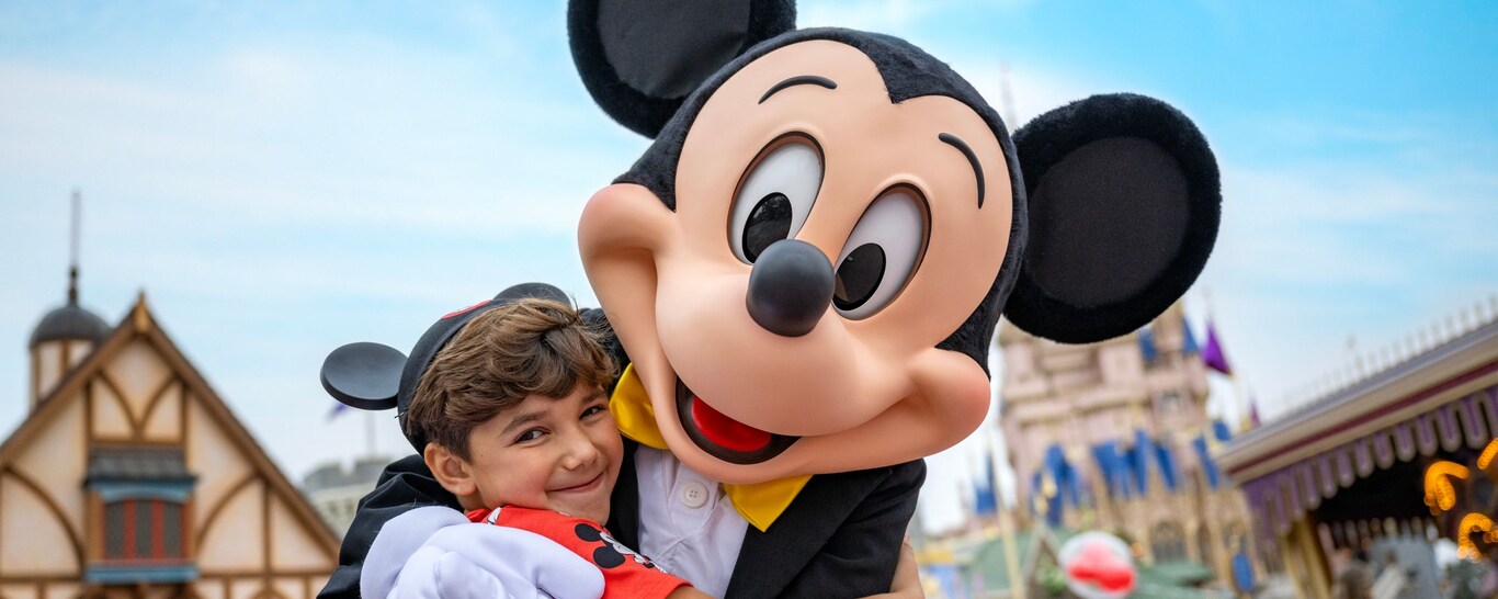 A child wearing a Mickey Mouse ear hat while hugging Mickey Mouse in Fantasyland at Magic Kingdom park