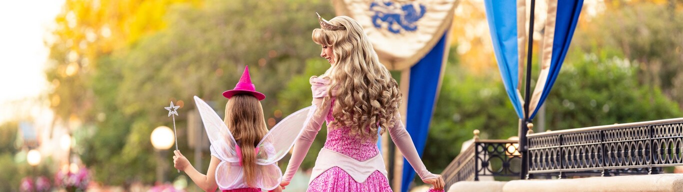 Princess Aurora walking with a young girl dressed as a fairy godmother.