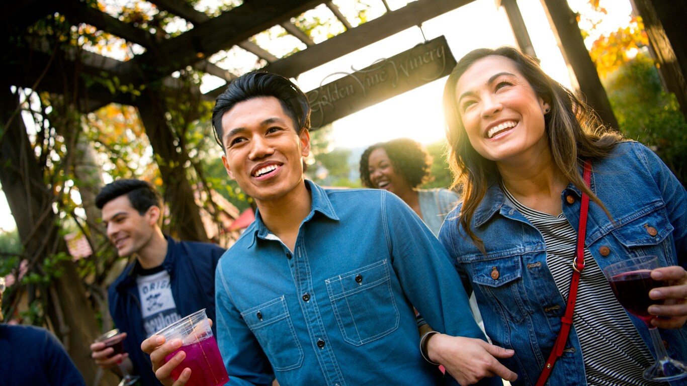 Una pareja joven sostiene unas bebidas mientras caminan debajo de un pérgola