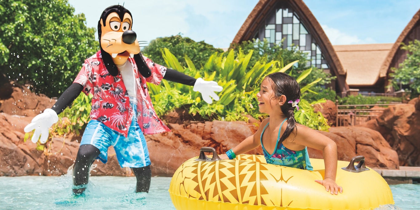 A girl inside an inner tube in a swimming pool laughs at Goofy, who wades in to greet her