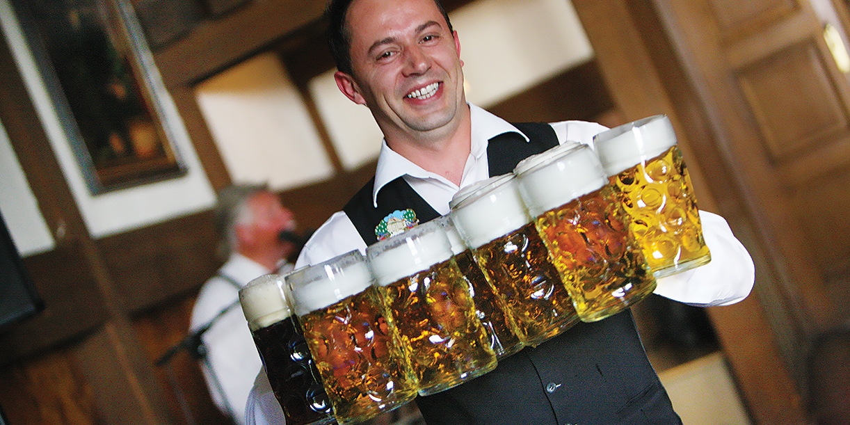 A man holding six large steins of beer