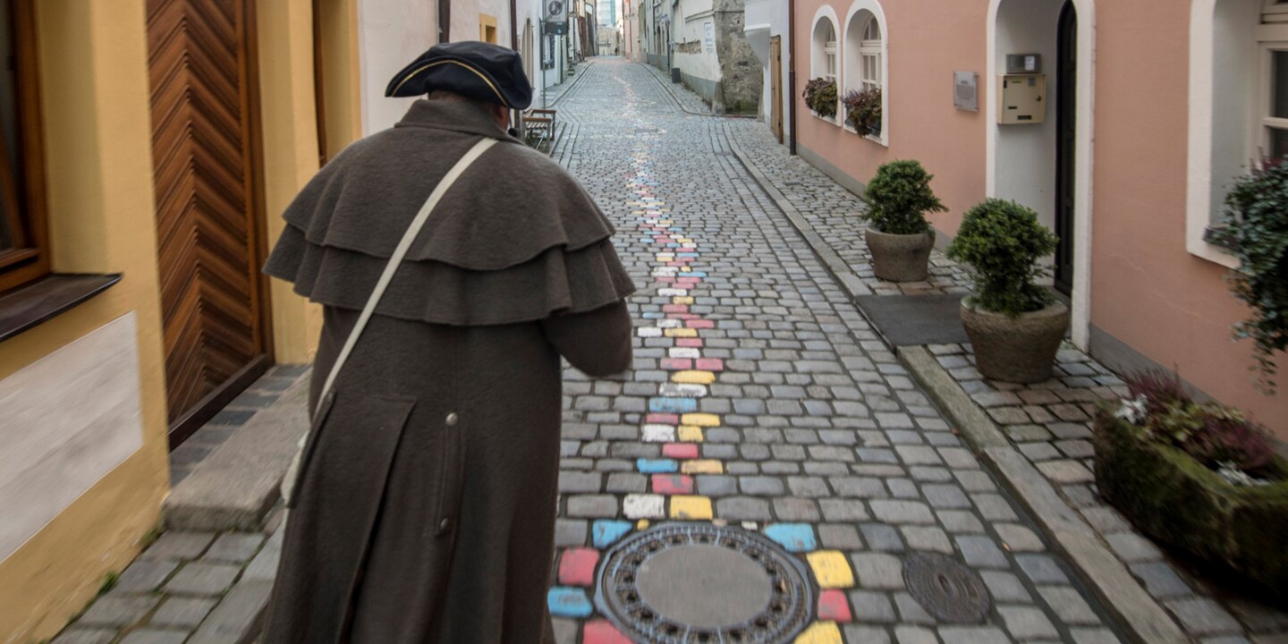 A man in a hat walks down a narrow, cobblestone street