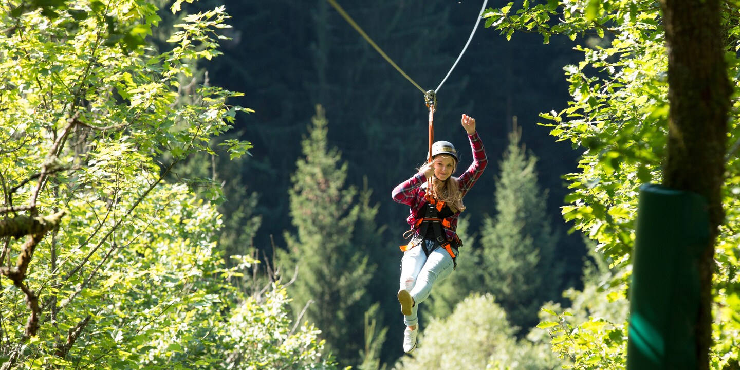 A girl waves as she ziplines through a forest
