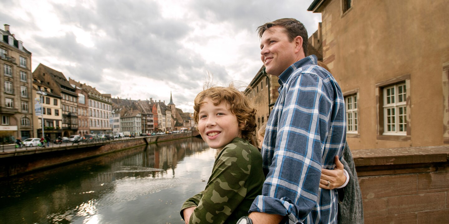 A family of 3 on a boardwalk overlooking a waterway in an old European town