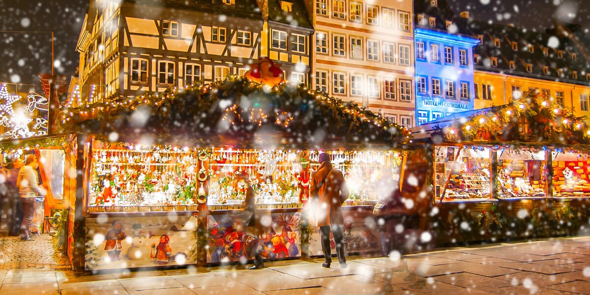 People shop the lit up stalls of a Christmas market on a snowy night in Strasbourg, France