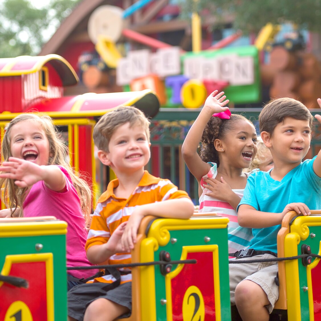 A half dozen young boys and girls smile and wave as they ride the Marketplace Train at Disney Springs