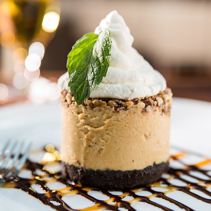 Celebrate a special occasion by dipping into our decadent desserts! slide 59 of 12 The Peanut Butter Snickers Pie topped with whipped cream and a sprig of mint on a plate drizzled with chocolate and caramel sauce