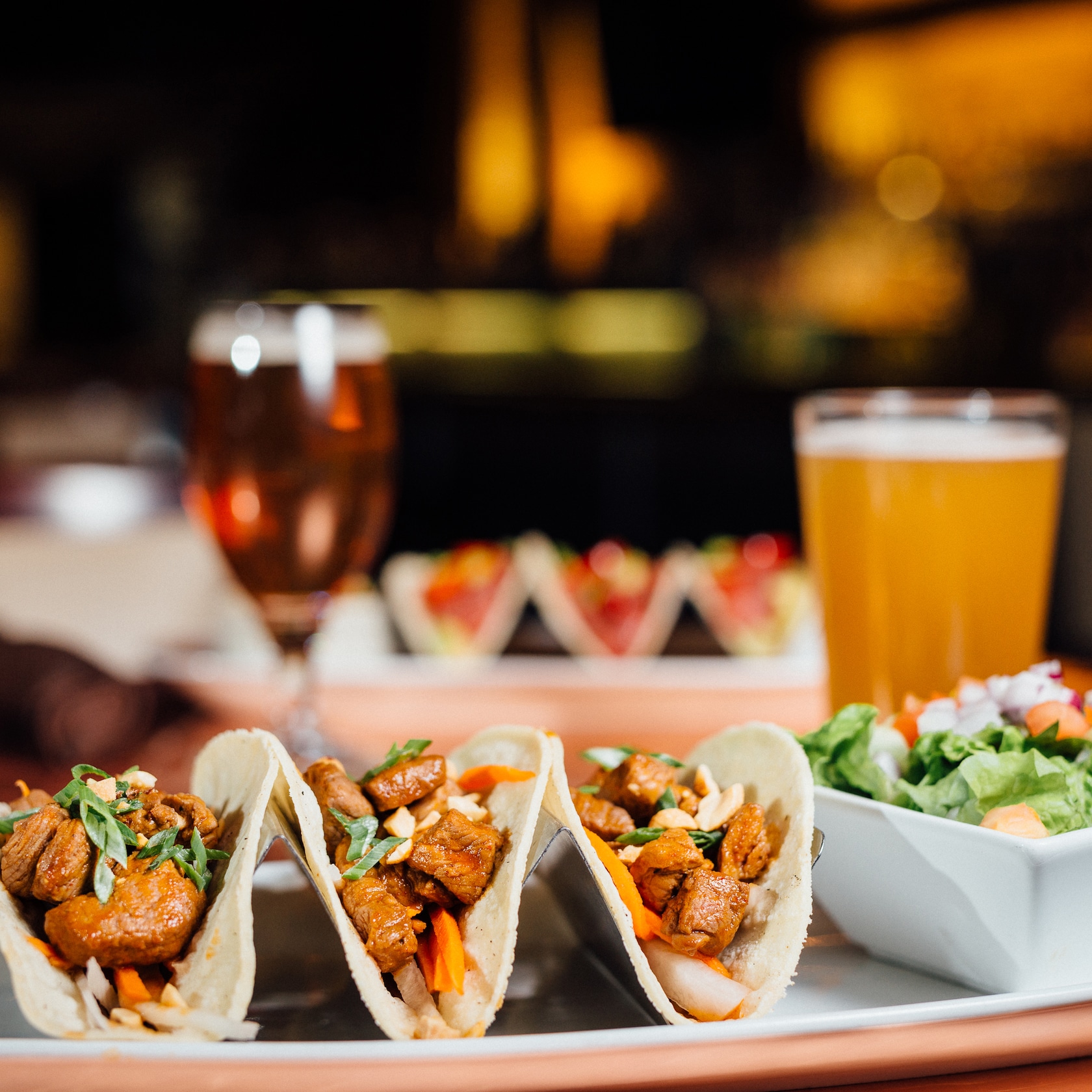 Come for the game—and stay for the scrumptious bites and sips! slide 50 of 12 A glass of draft beer and a platter featuring 3 Short Rib Tacos and a salad