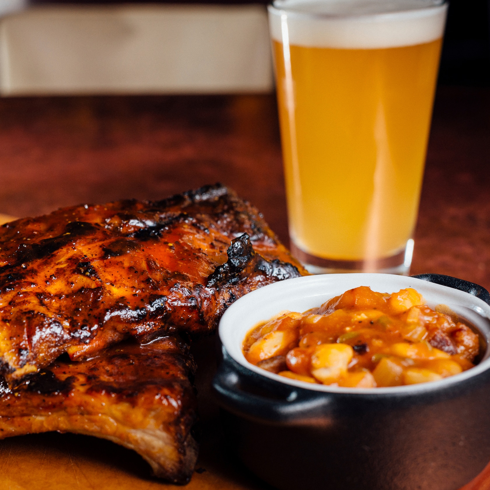 undefined slide 52 of 12 BBQ ribs served with baked beans and creamed corn in casserole style dishes and draft beer in a glass
