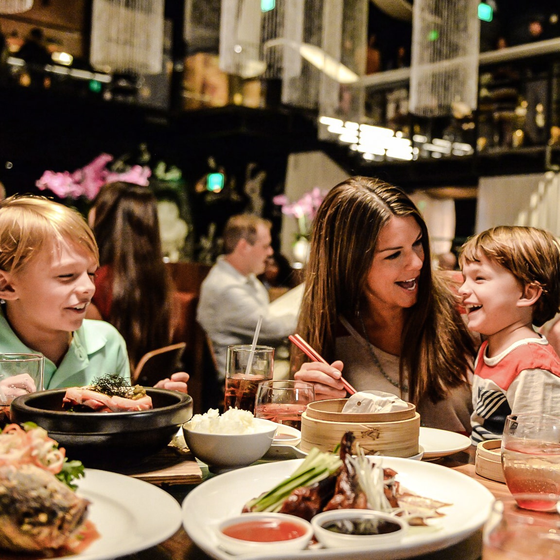 A mother and her 2 children smile while eating in a modern dining room at Morimoto Asia