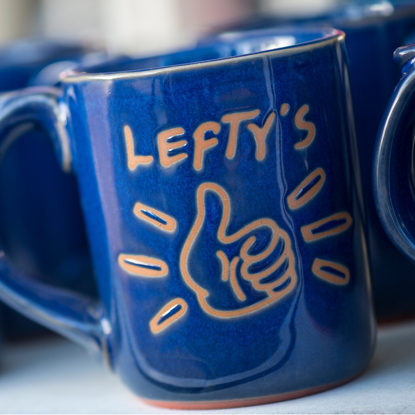 Logo terra-cotta left-handed mugs on a shelf within Lefty’s The Left Handed Store at Disney Springs