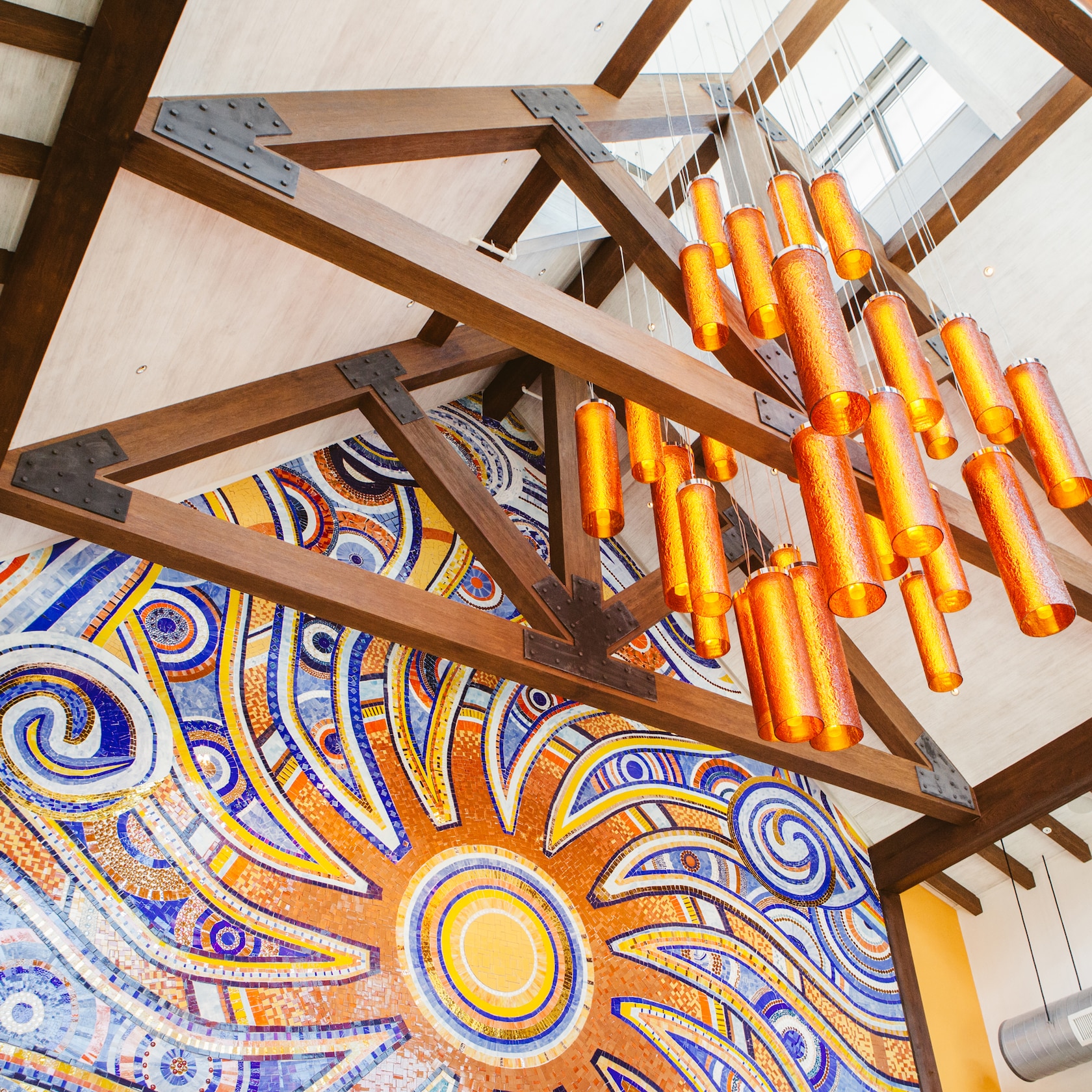 Warm accents enhance the lively ambiance of this upscale Mexican restaurant. slide 76 of 16 Cylinder lights dangling from a ceiling beam in front of a vibrant wall mural