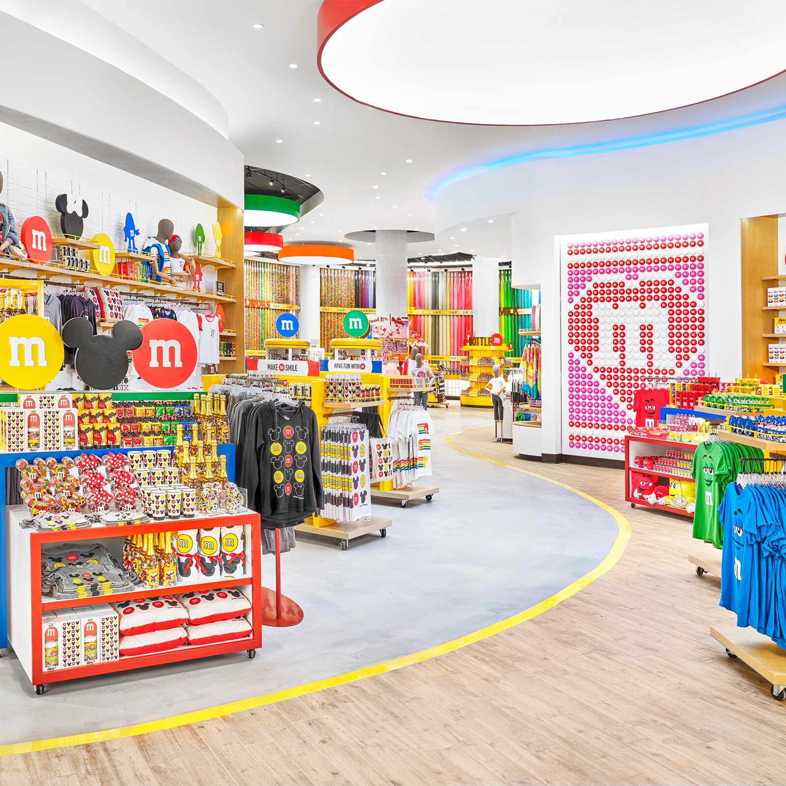 A store filled with M and M merchandise, including cups, shirts, towels, pillows and tall cylinders of candy. The display racks have labels that read Make M Smile and Have Fun with M.