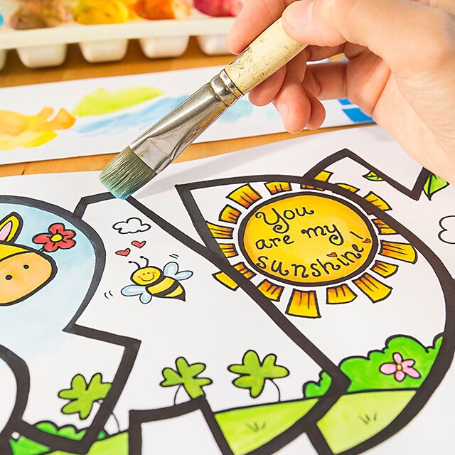A hand holding a paintbrush, coloring a whimsical meadow scene contained by the outline of the letters of the name Brady