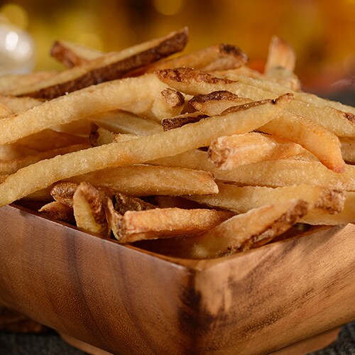 Papas fritas crujientes dentro de un tazón de madera, servidas con distintas salsas
