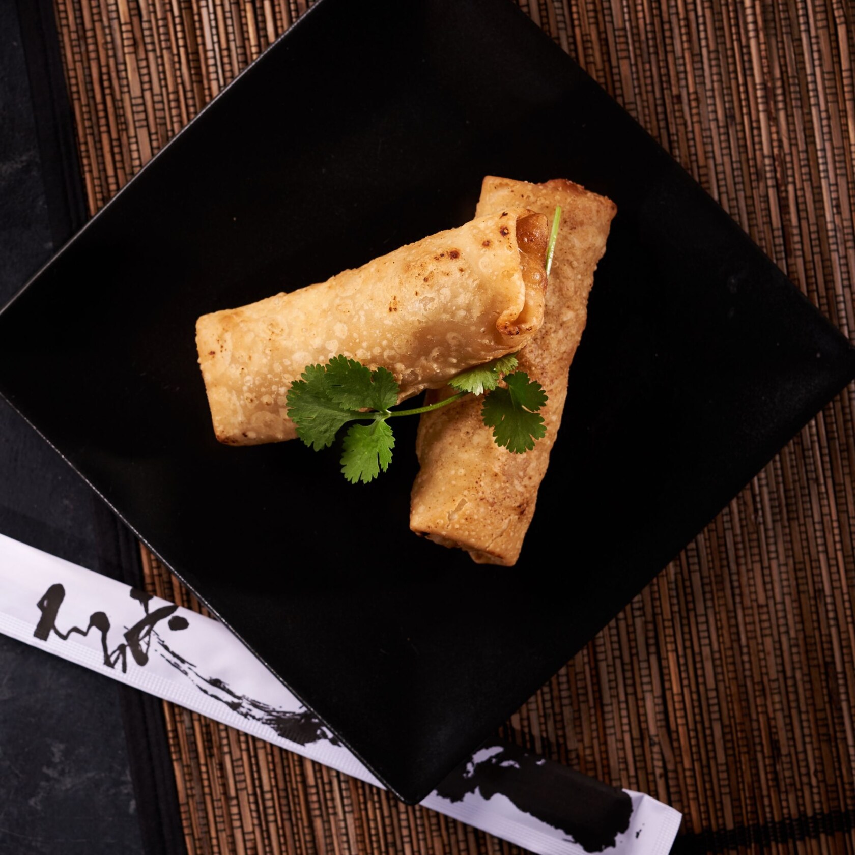 A pair of pork egg rolls and chopsticks displayed on a bamboo placemat