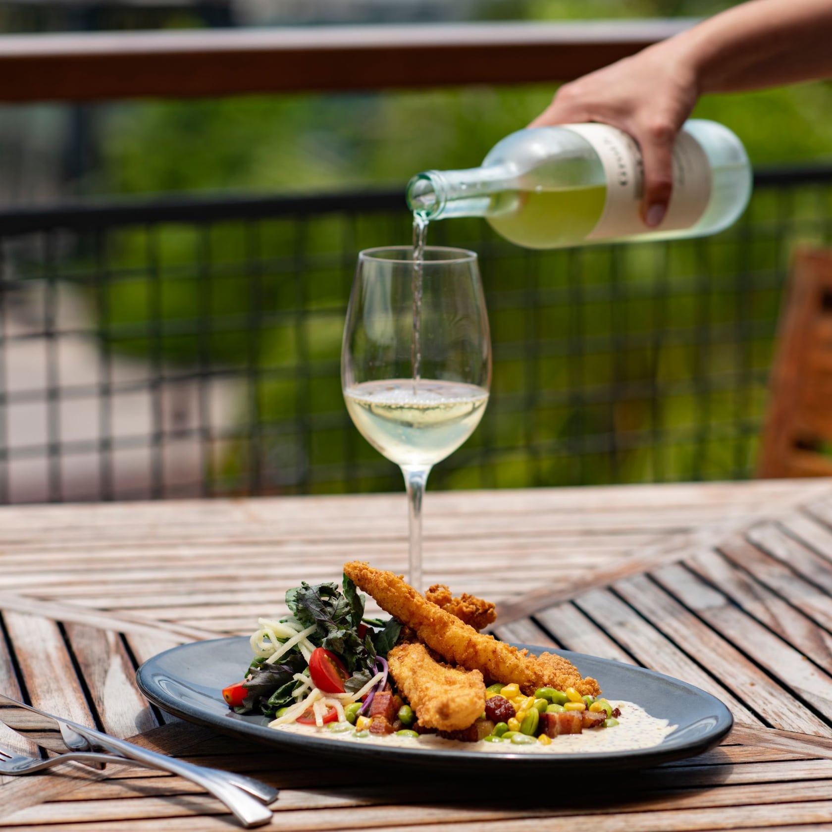 Pair your meal with a crisp glass of wine, or select from a wide variety of beverage options. slide 28 of 6 At an outdoor table, a hand pours wine into a glass, which is next to a tempting plate of catfish and succotash