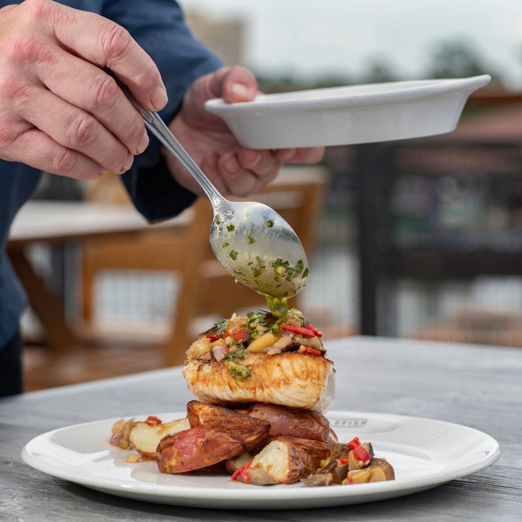 Feast on exquisitely prepared dishes. slide 29 of 6 A man’s hand spoons salsa verde over a piece of Mahi, which rests on a bed of potatoes