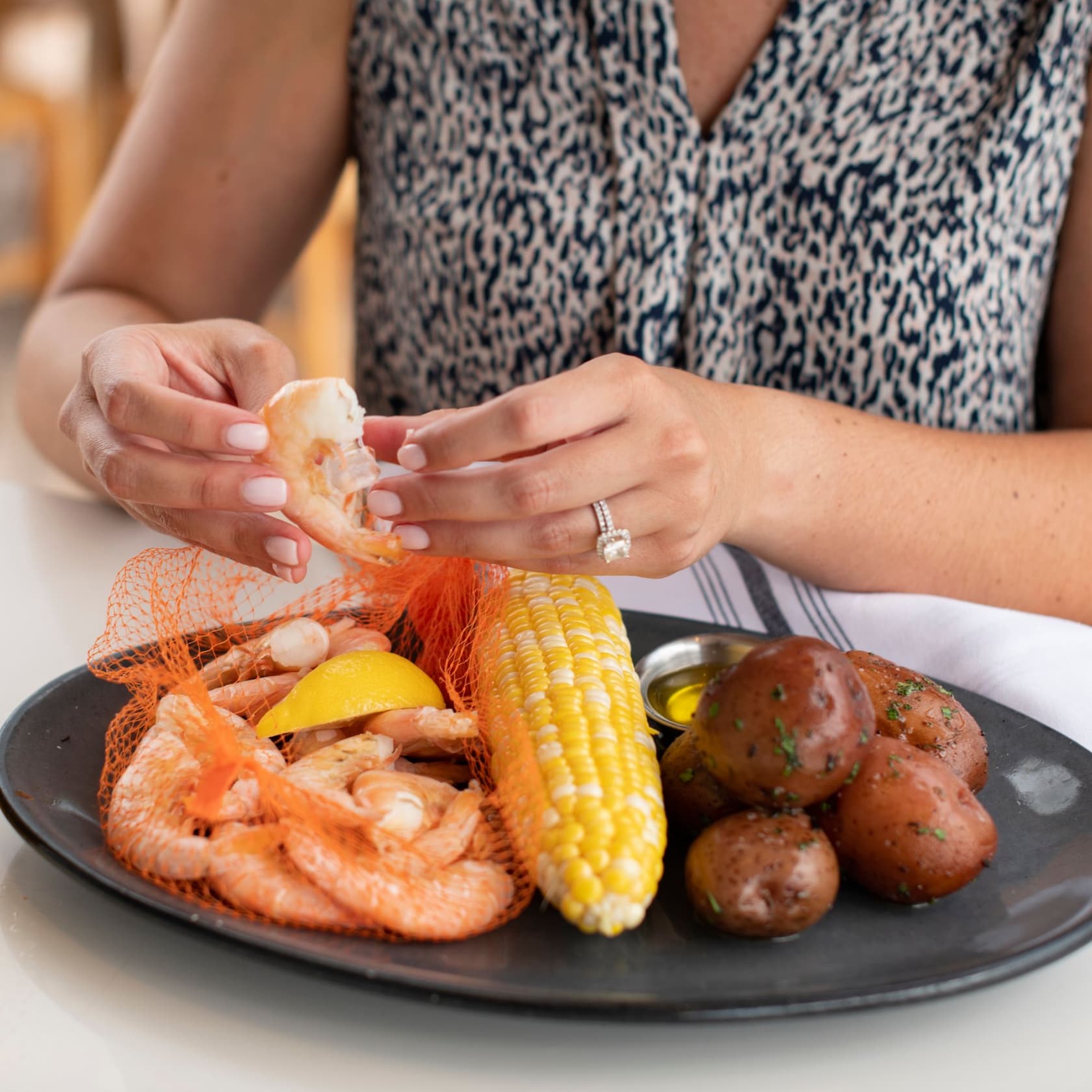 Delight in Peel & Eat Key West Pink Shrimp, with sides of potatoes and corn on the cob. slide 26 of 6 A woman peels a shrimp as she sits before a plate of Key West shrimp, potatoes and corn on the cob