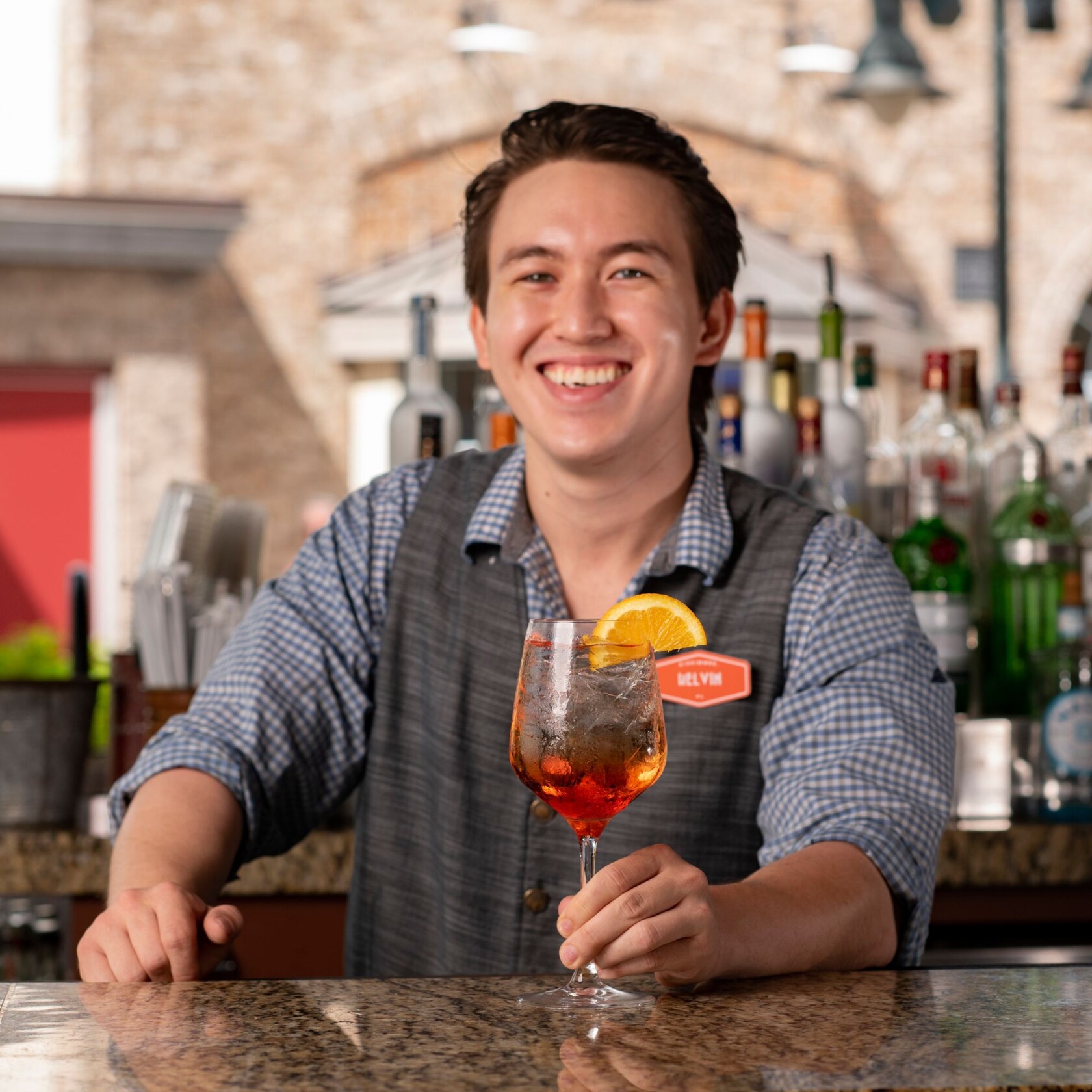 A smiling bartender holding a beverage at an outside bar