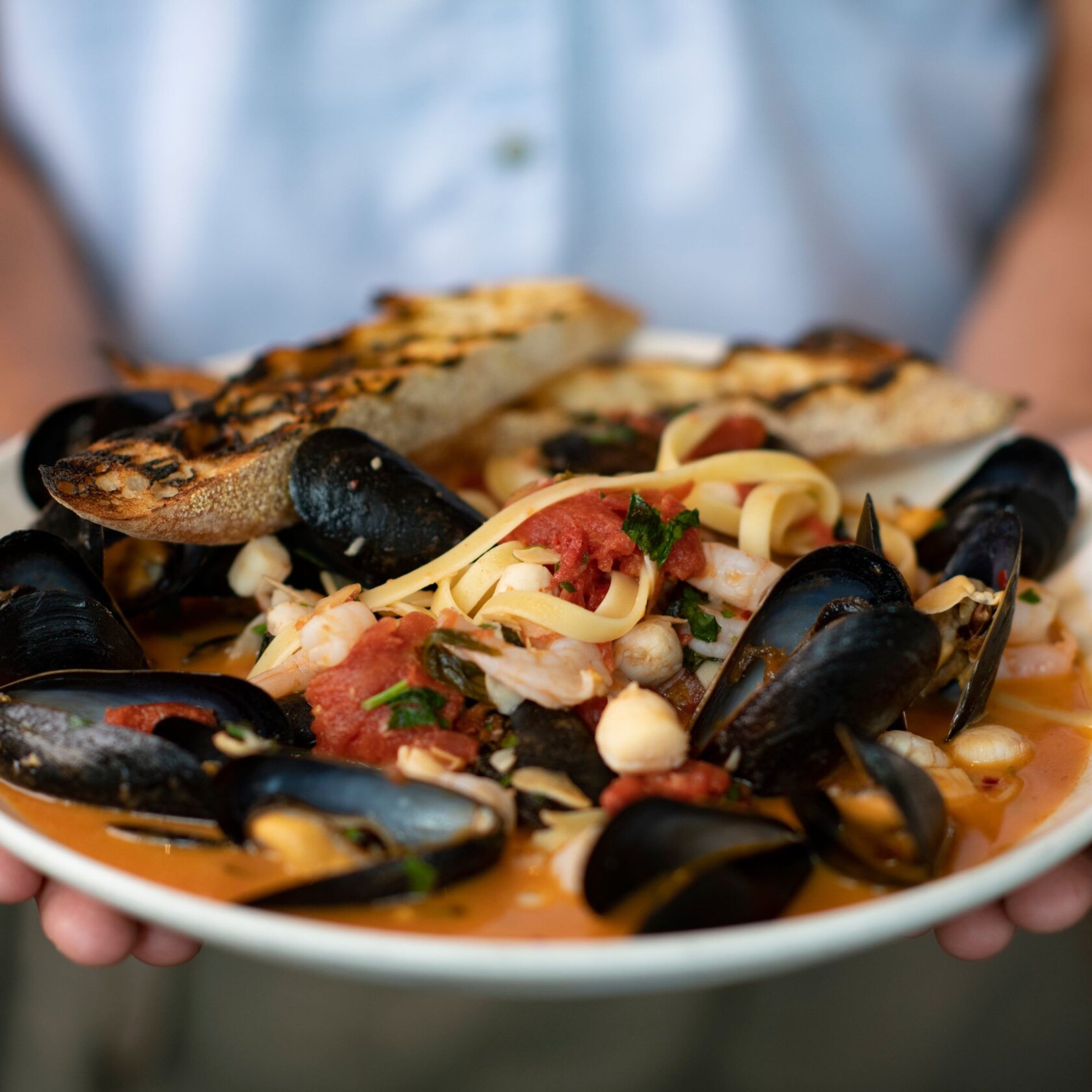 A server holding a bowl of pasta with mussels and shrimp