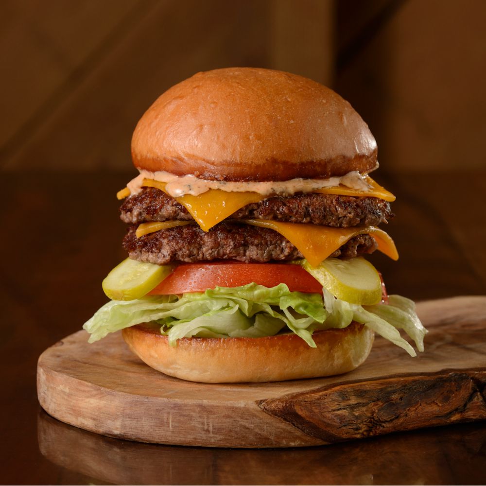 Una hamburguesa con queso con 2 hamburguesas, queso, pepinillos, tomate, lechuga y salsa