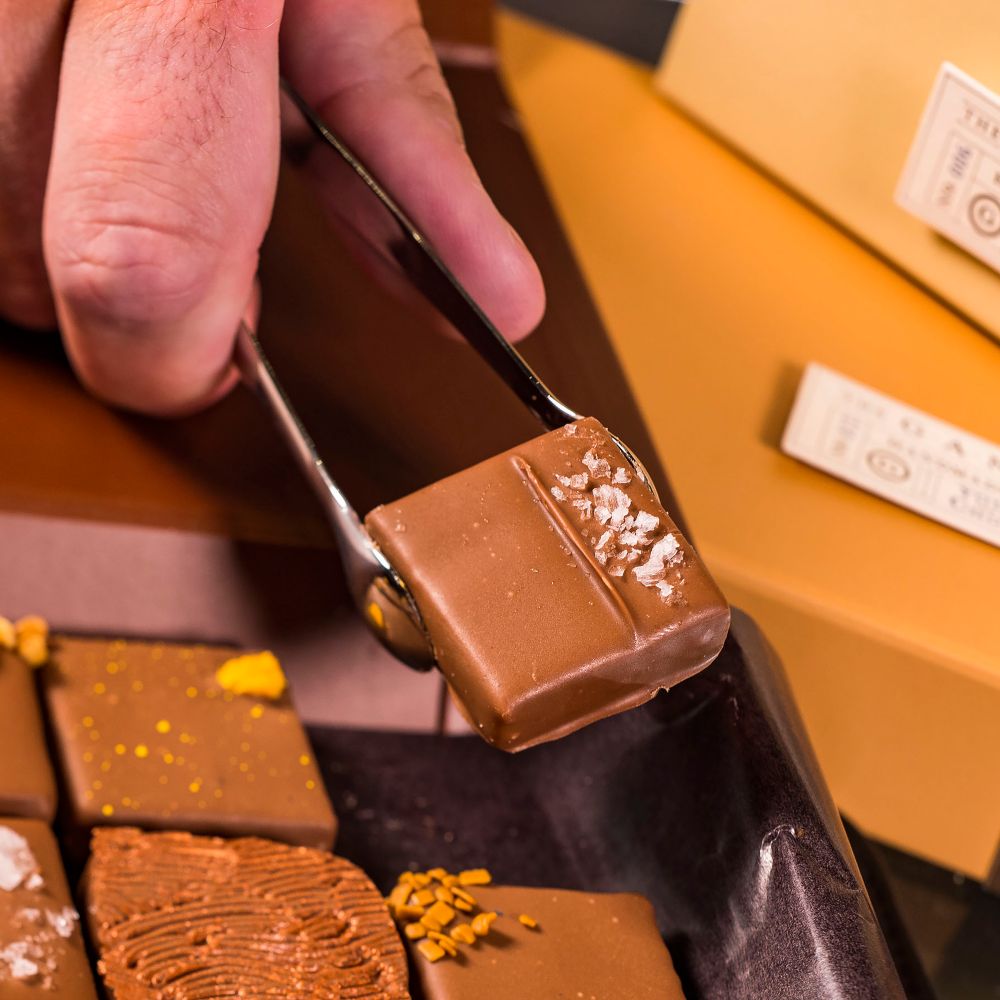 Savor a blissful bite of ganache—or select an assortment to take home. slide 21 of 5 A ganache square being picked up with tongs