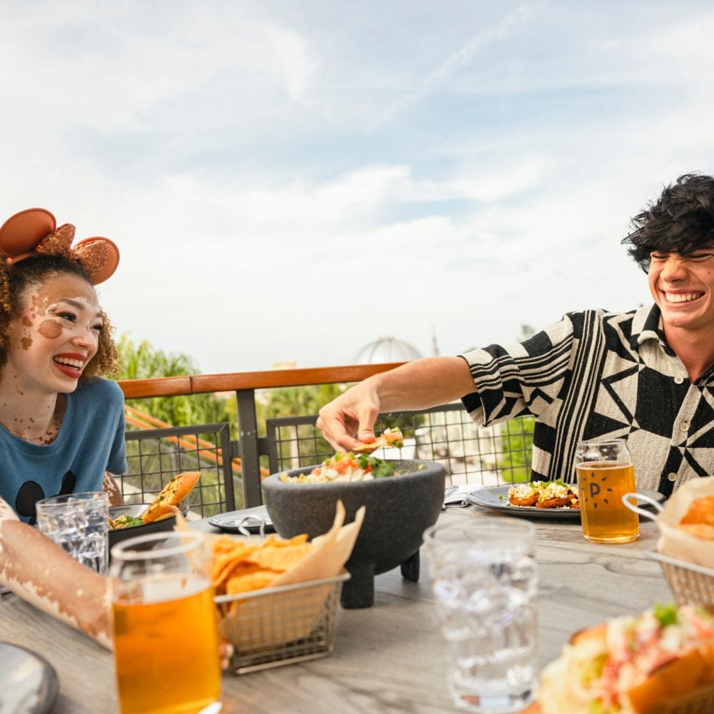 Enjoy incredible views of Disney Springs while dining aboard a steamboat at Paddlefish. slide 25 of 6 Two Guests enjoying food and beverages while sitting on an outdoor deck at Paddlefish