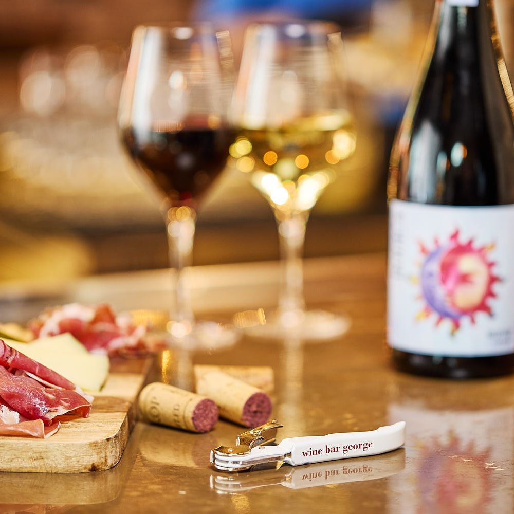 Glasses of wine, 2 bottles of wine, a charcuterie board and a wine key that says, 'Wine Bar George'