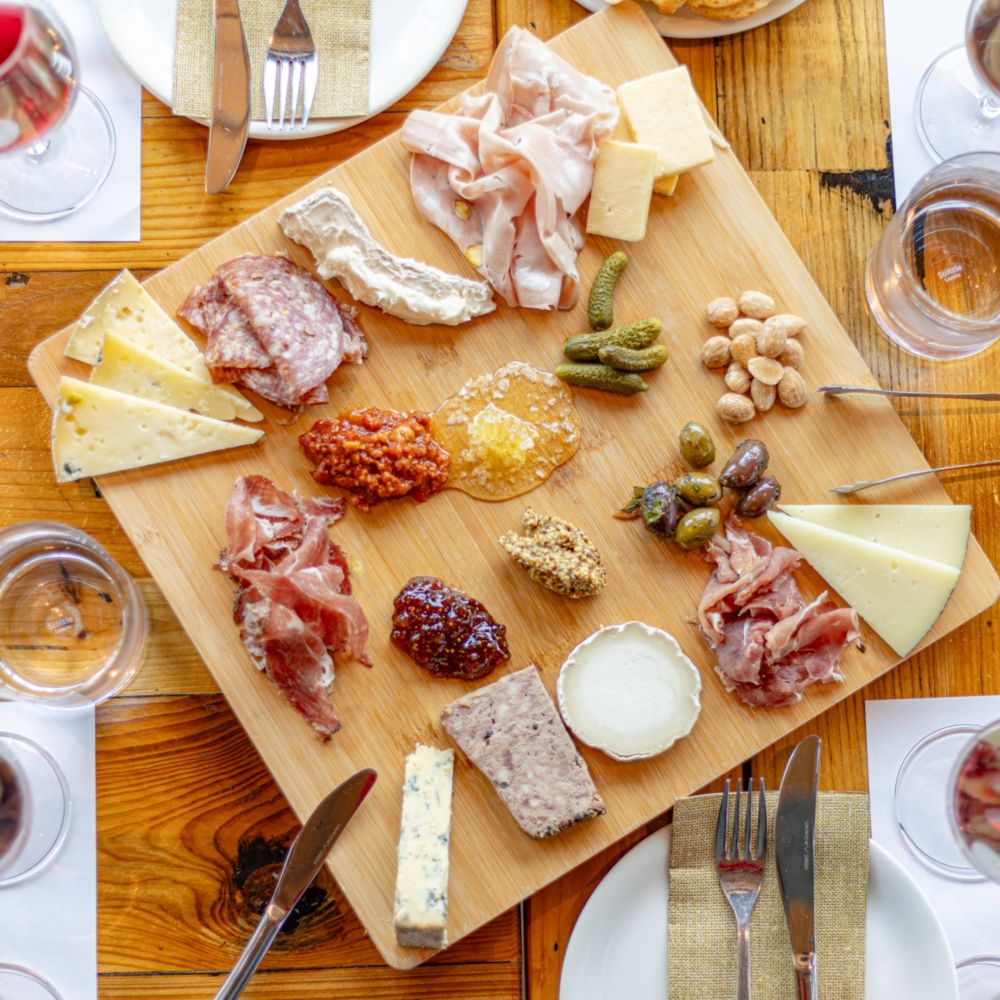 An overhead view of a large charcuterie board surrounded by 4 wine tasting settings