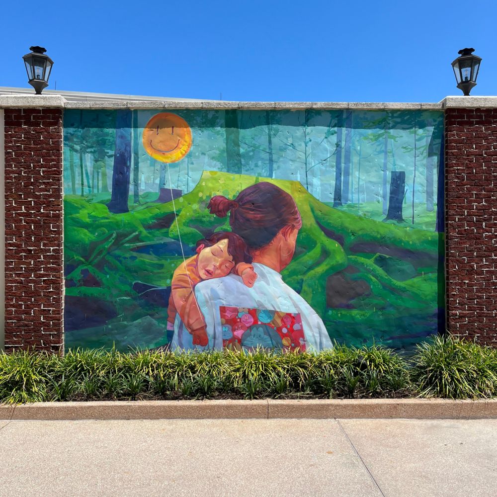 A mural of a mother walking through a forest while she holds her sleeping son 