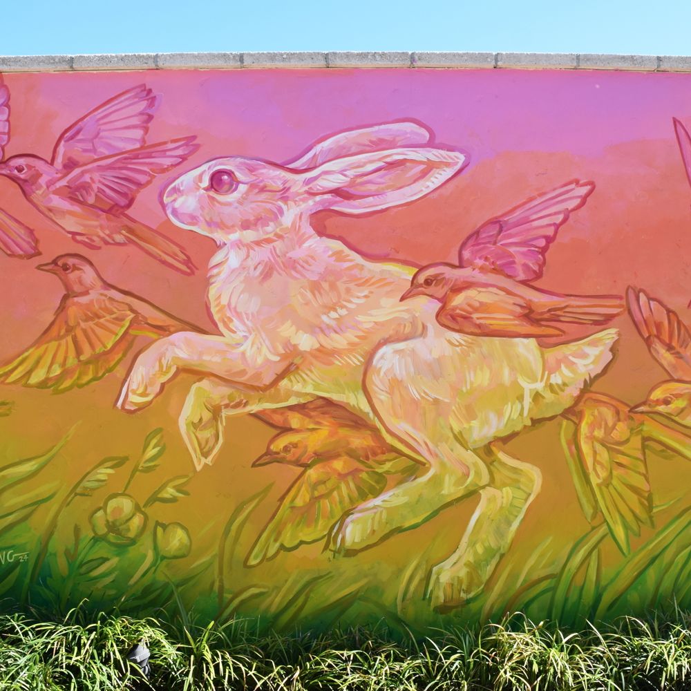 A mural against a brick wall by artist Emily Ding featuring a rabbit surrounded by birds, set against a gradient background