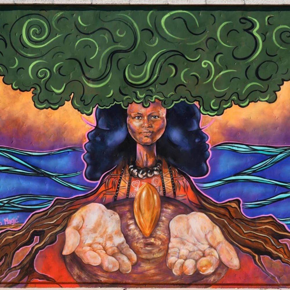 A mural of a woman with tree like hair with open hands holding a seed