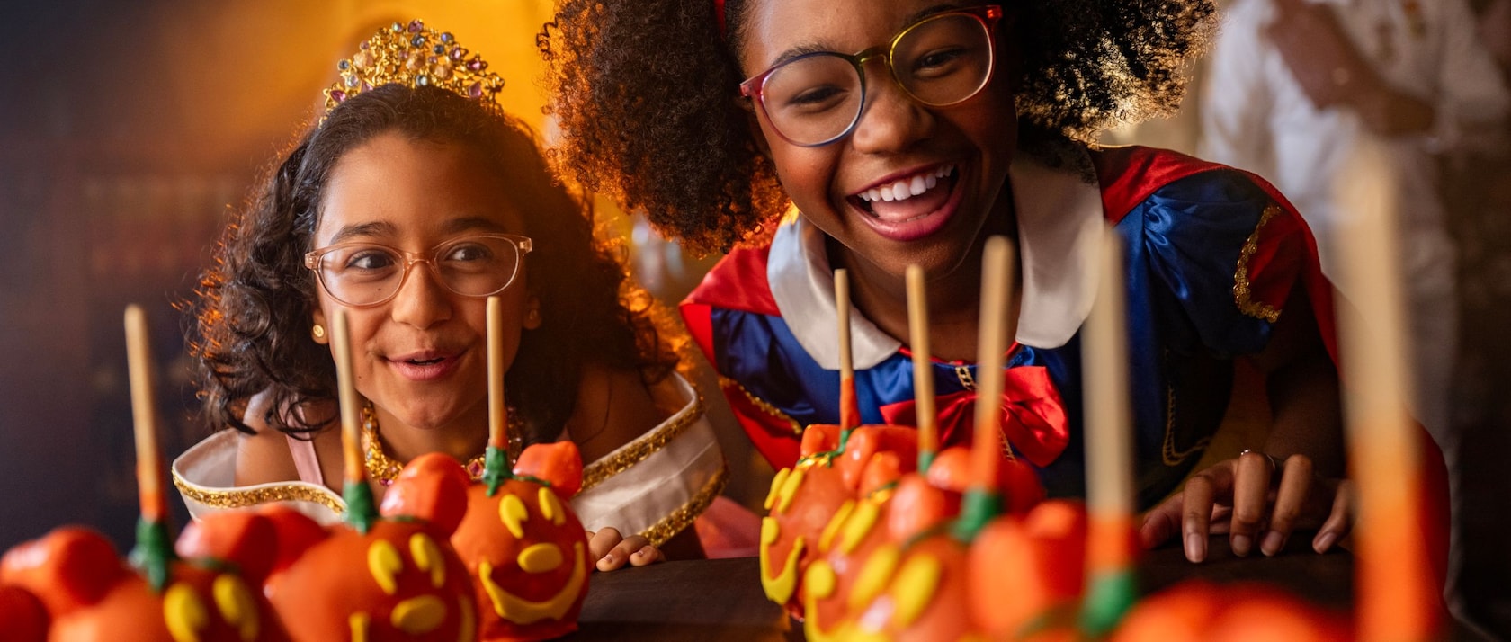 Two girls dressed as Snow White and Aurora looking at Halloween themed Mickey Mouse candy apples