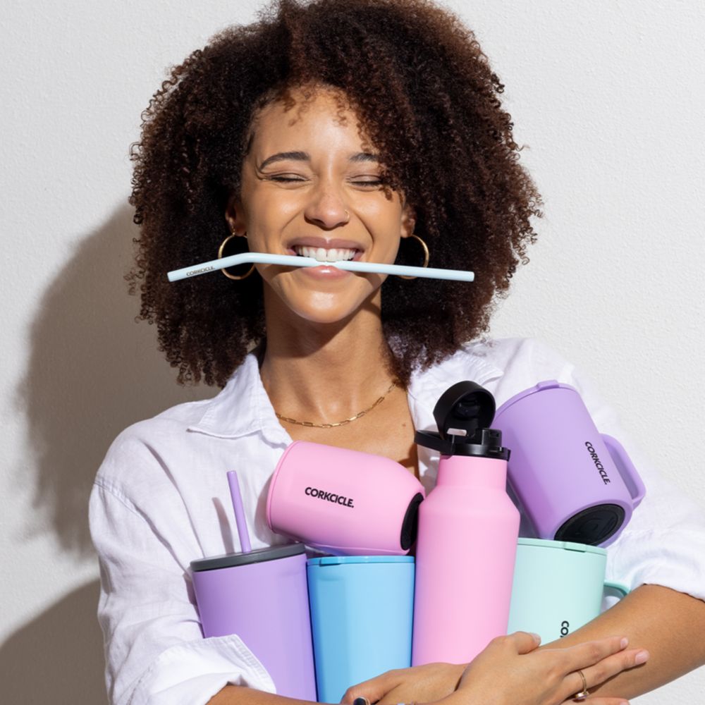 Una joven sonriente sosteniendo una variedad de recipientes para bebidas Corkcicle	