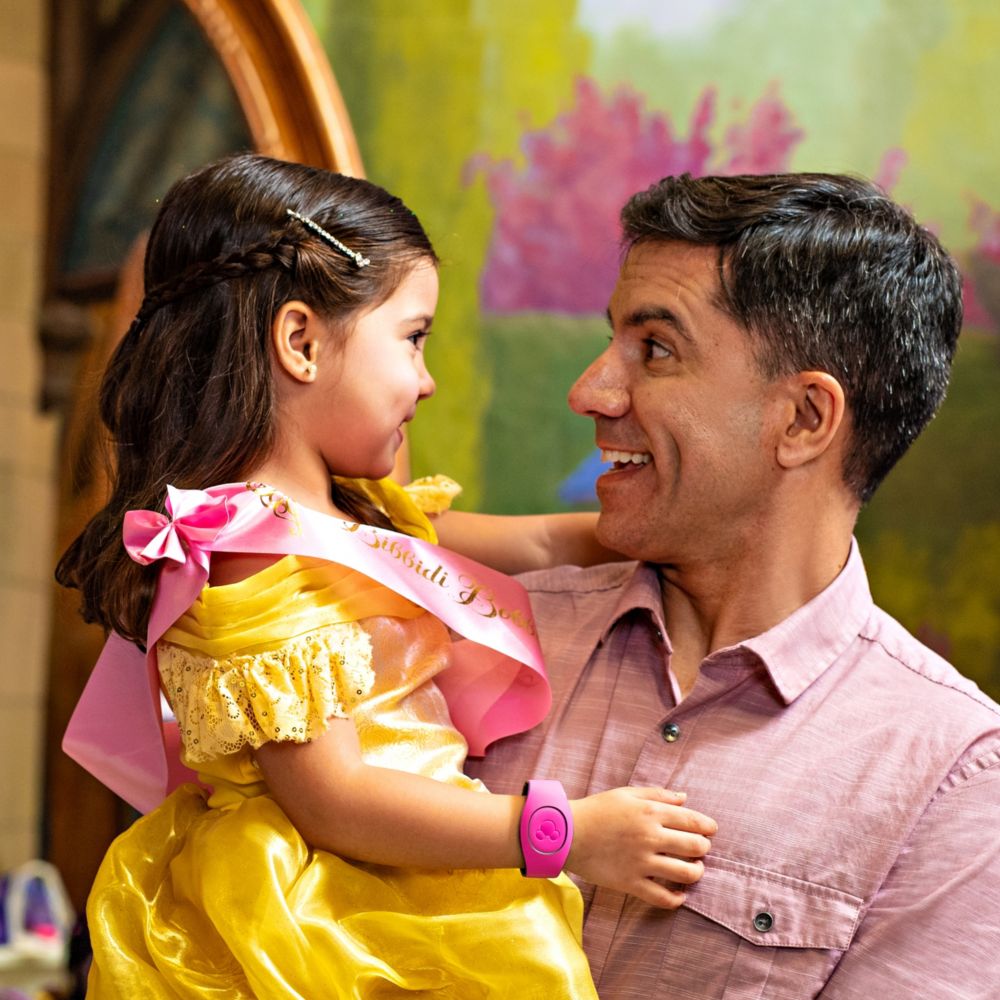 A father smiling and holding his young daughter who is wearing a princess makeover at the Bibbidi Bobbidi Boutique at Disney Springs