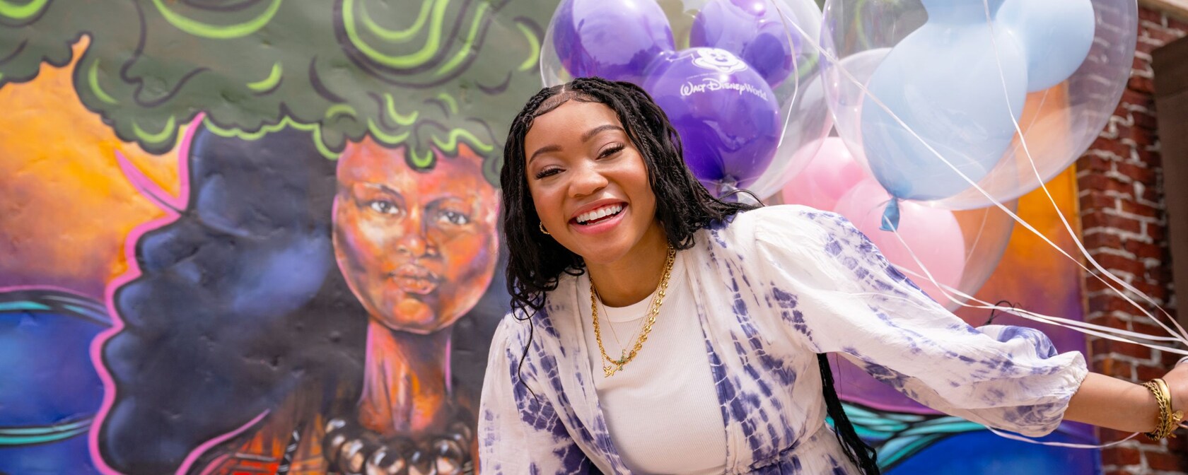 A woman holding Mickey Mouse shaped balloons in front of a mural