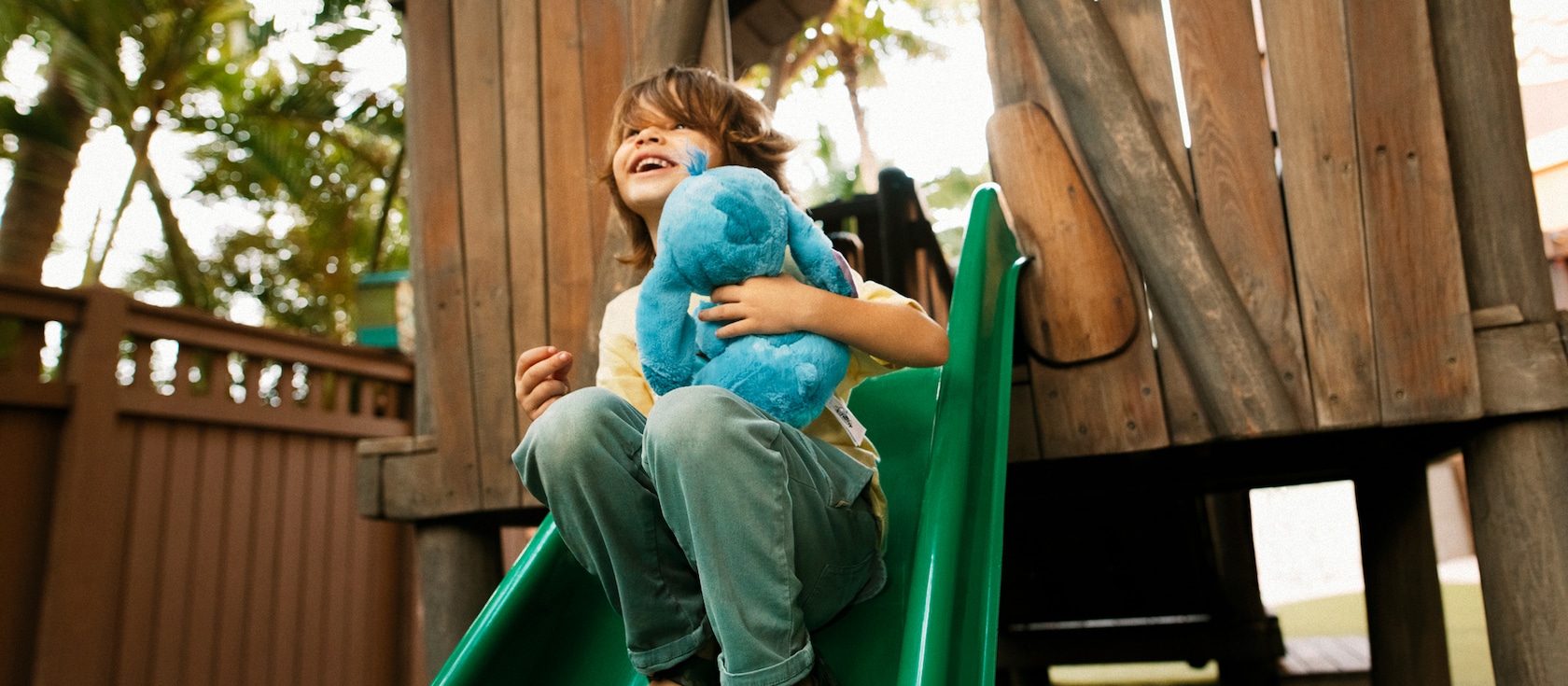 A young boy goes down a slide holding a Stitch plush