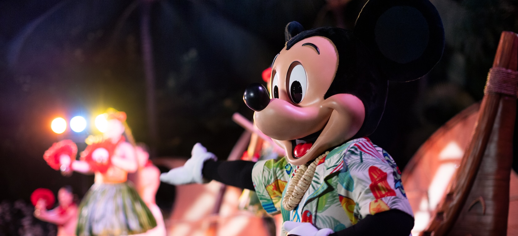Mickey Mouse, wearing a Hawaiian shirt and a shell lei, joins performers on stage at night