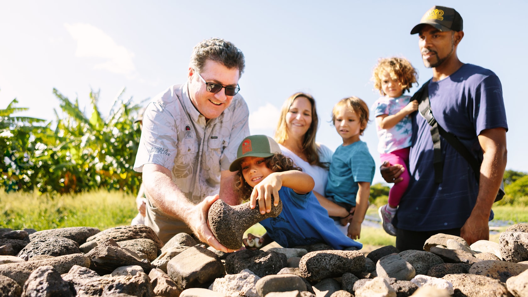 Adults and kids look at a pile of rocks, fascinated by a lava rock with a distinctive shape